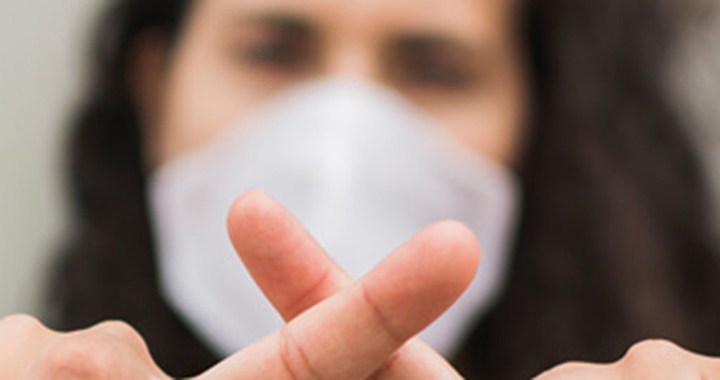 A woman wearing a face mask making the x sign, indicating a gesture of refusal or disagreement