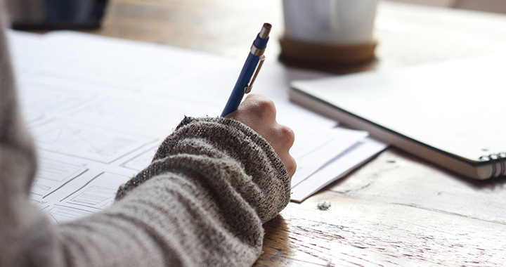 A person writing on paper with a pen